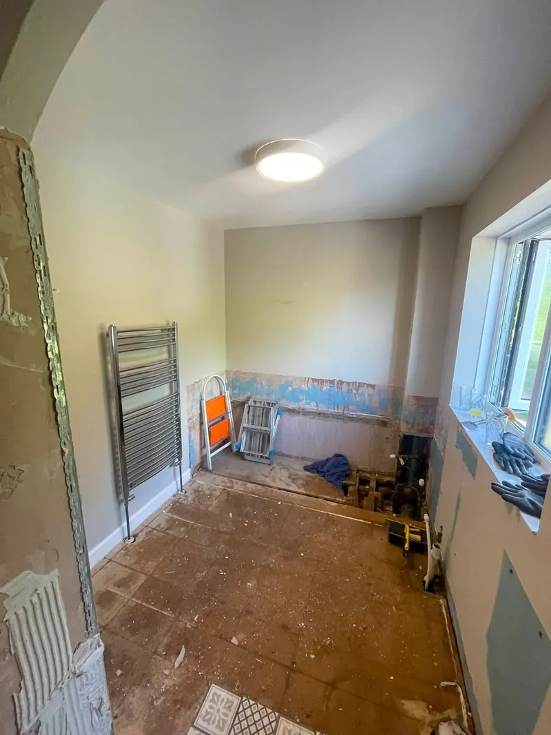 Bathroom before renovation: stripped back to bare floorboards with exposed pipework and damaged plaster